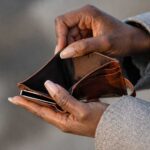 Mains d’une personne tenant un portefeuille vide, illustrant la perte de pouvoir d’achat et la vie chère en Haïti.