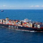Navire porte-conteneurs en mer avec le mot Haïti sur la coque, illustrant le commerce maritime et les recettes douanières.