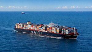 Navire porte-conteneurs en mer avec le mot Haïti sur la coque, illustrant le commerce maritime et les recettes douanières.