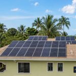 Maison équipée de panneaux solaires entourée de cocotiers, illustrant les solutions solaires individuelles en Haïti.