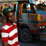 Un homme devant un tap-tap coloré en Haïti, illustrant la hausse des coûts du transport.