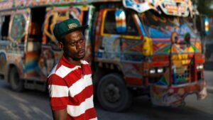 Un homme devant un tap-tap coloré en Haïti, illustrant la hausse des coûts du transport.