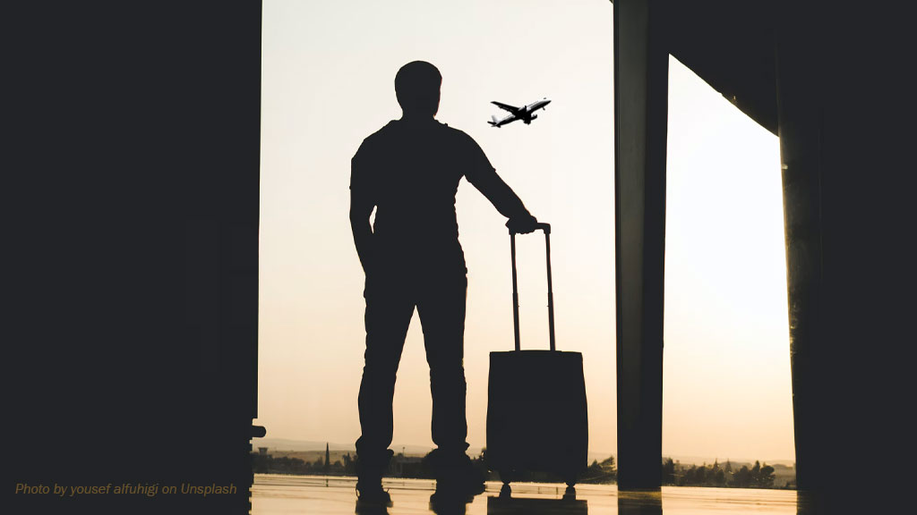 Silhouette d’un voyageur avec une valise dans un aéroport, devant un avion en vol, illustrant un possible retour en Haïti après la fin du TPS.