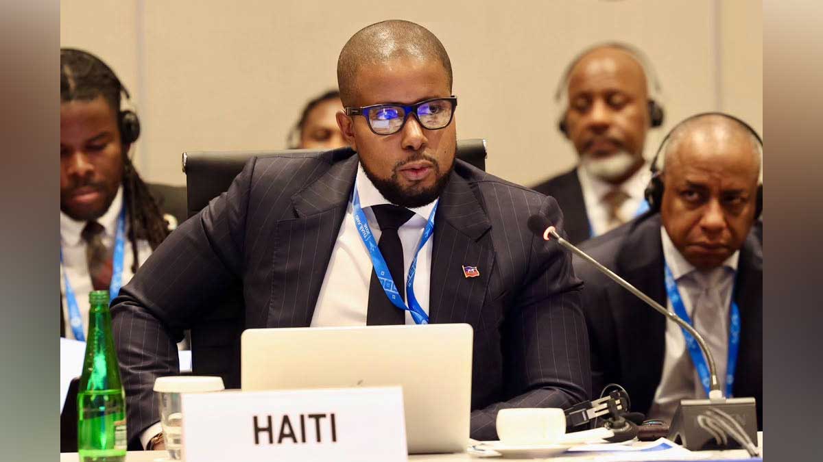 Le ministre haïtien de l’Économie et des Finances, Serge Gabriel Collin, prend la parole lors d’une réunion internationale, derrière une pancarte portant l’inscription « HAITI ».